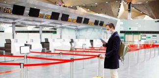 Traveler wearing a mask stands by yellow suitcase at empty airport check-in