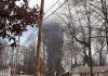 Suburban street with large plume of dark smoke rising beyond trees