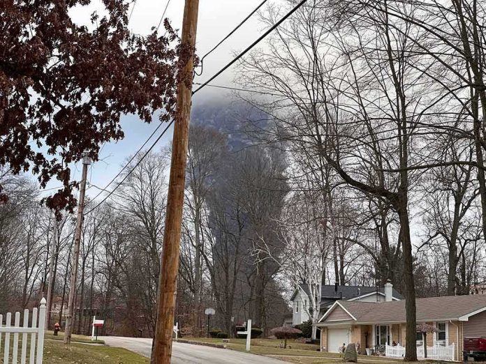 shutterstock_2262459999 Suburban street with large plume of dark smoke rising beyond trees