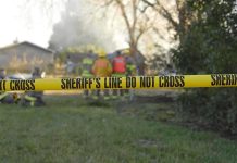 Capital Murder Shock: Sons Found, Gun Nearby Yellow police tape marking a restricted area at a fire scene with firefighters in the background