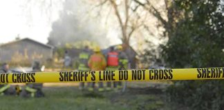 Capital Murder Shock: Sons Found, Gun Nearby Yellow police tape marking a restricted area at a fire scene with firefighters in the background