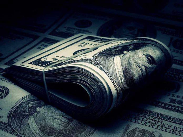 shutterstock_125542373.jpg A rolled stack of hundred dollar bills on a background of more banknotes