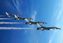 Four military jets flying in formation against a blue sky leaving smoke trails