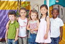 Five children standing together in a playground setting smiling at the camera