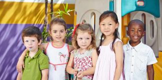 Five children standing together in a playground setting smiling at the camera